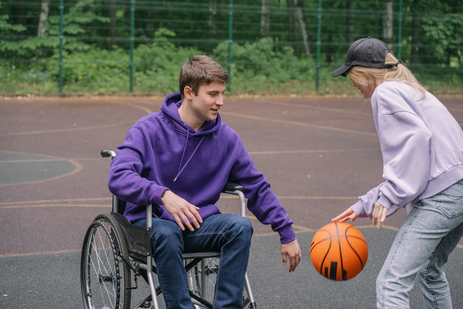 A wheelchair user playing basketball outdoors with a friend